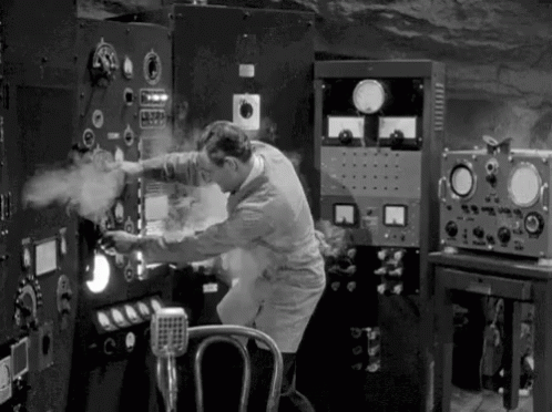 A GIF of a scientist turning dials of a machine that has smoke coming out of it in black and white.