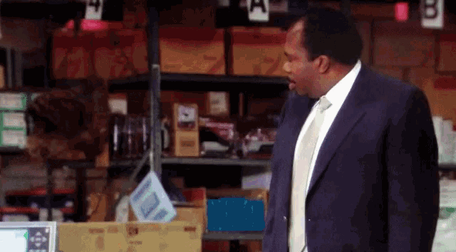 A GIF of a man in a suit raising his fist in a warehouse with a smile on his face.